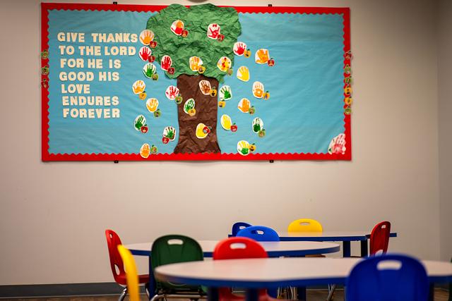 “Give thanks to the Lord” bulletin board above colourful tables and chairs