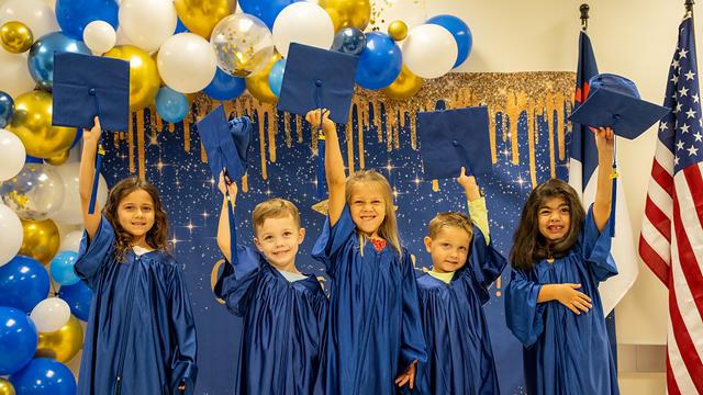 Class of 2026 graduates in blue gowns tossing their caps in the air