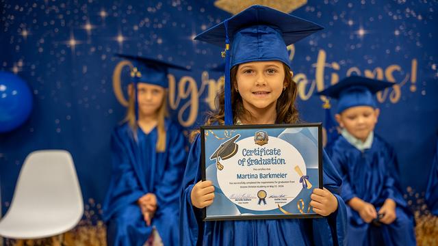 A smiling graduate in a blue cap holding a certificate of graduation