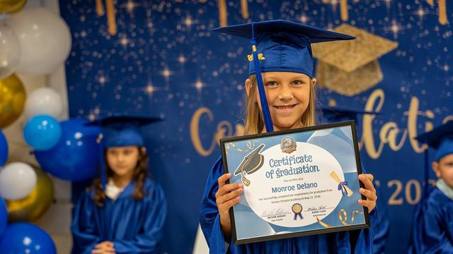 A graduate grinning behind a framed certificate of graduation