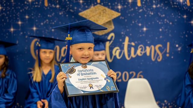 A graduate with a big smile holding a certificate in front of the Congratulations backdrop