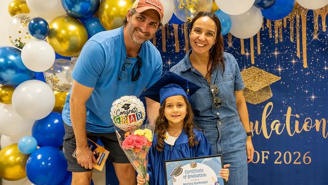 A graduate holding flowers and a “Congrats Grad” balloon with two grown-ups
