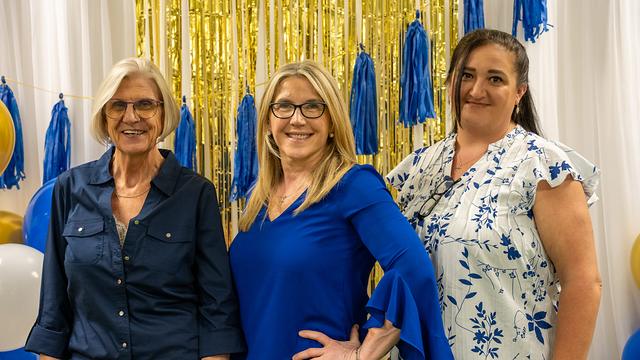 Three women smiling in front of gold streamers at the graduation celebration