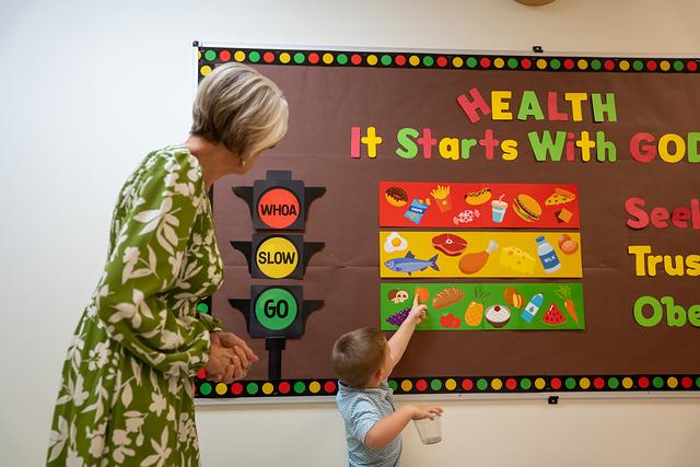 A little boy pointing at the “Health: It Starts With God” bulletin board