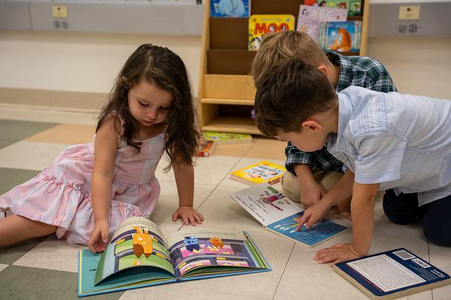 Three children looking through picture books on the classroom floor