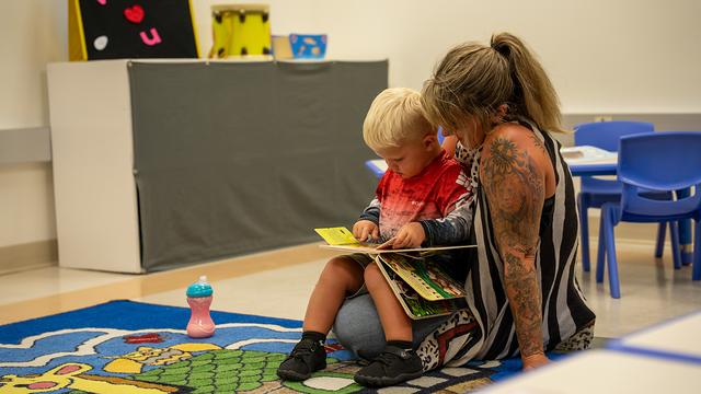 A parent reading a picture book with a little boy on the classroom rug