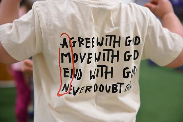 The back of a child’s T-shirt that reads “Agree with God, move with God, end with God, never doubt God”