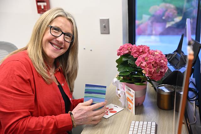 A smiling staff member at her desk with pink flowers and handmade cards