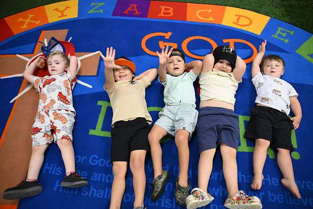 Five children lying on a “God Is Love” rug with their arms in the air