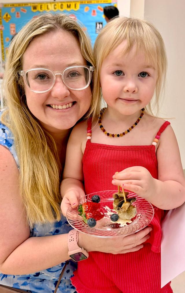 A smiling woman and a little girl in a red dress holding a plate of fruit