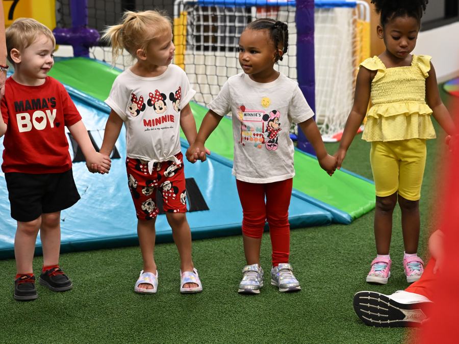 Four children holding hands in a line in the indoor play area