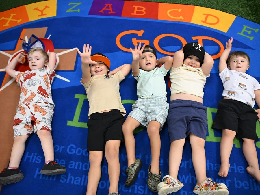 Five children lying on the &ldquo;God Is Love&rdquo; classroom rug with their hands in the air