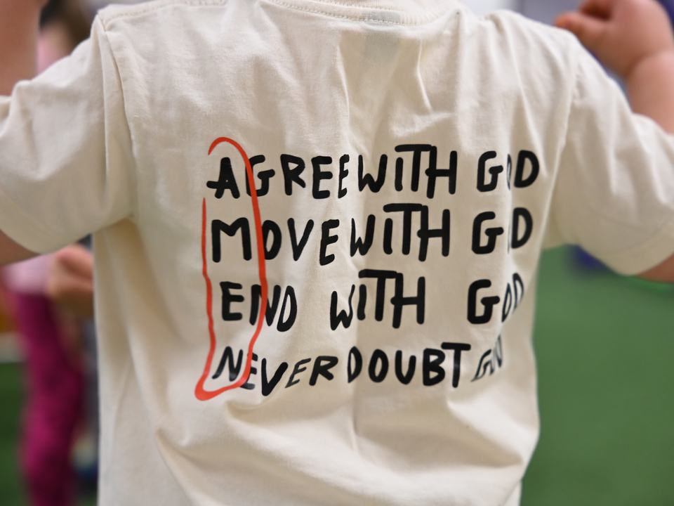 The back of a child’s T-shirt reading: Agree with God, move with God, end with God, never doubt God