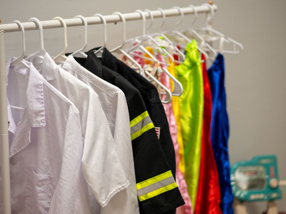 A dress-up rack with a doctor’s coat, a firefighter jacket and colorful capes