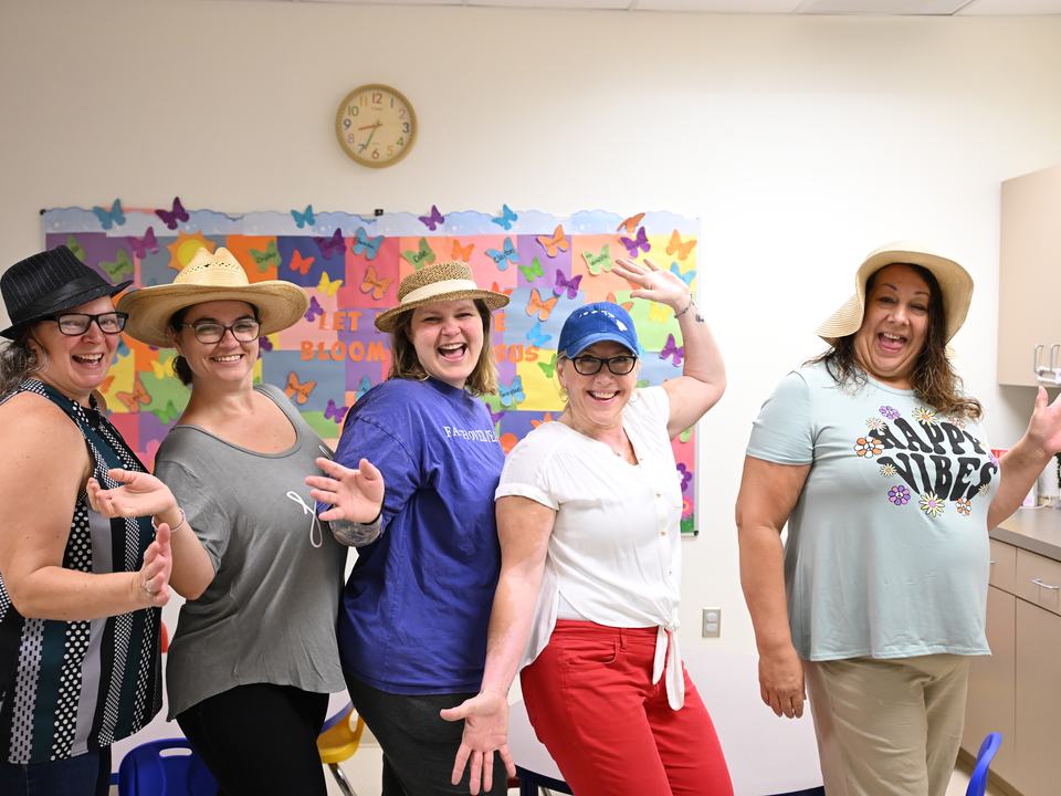 Teachers in sun hats striking a fun pose in a classroom
