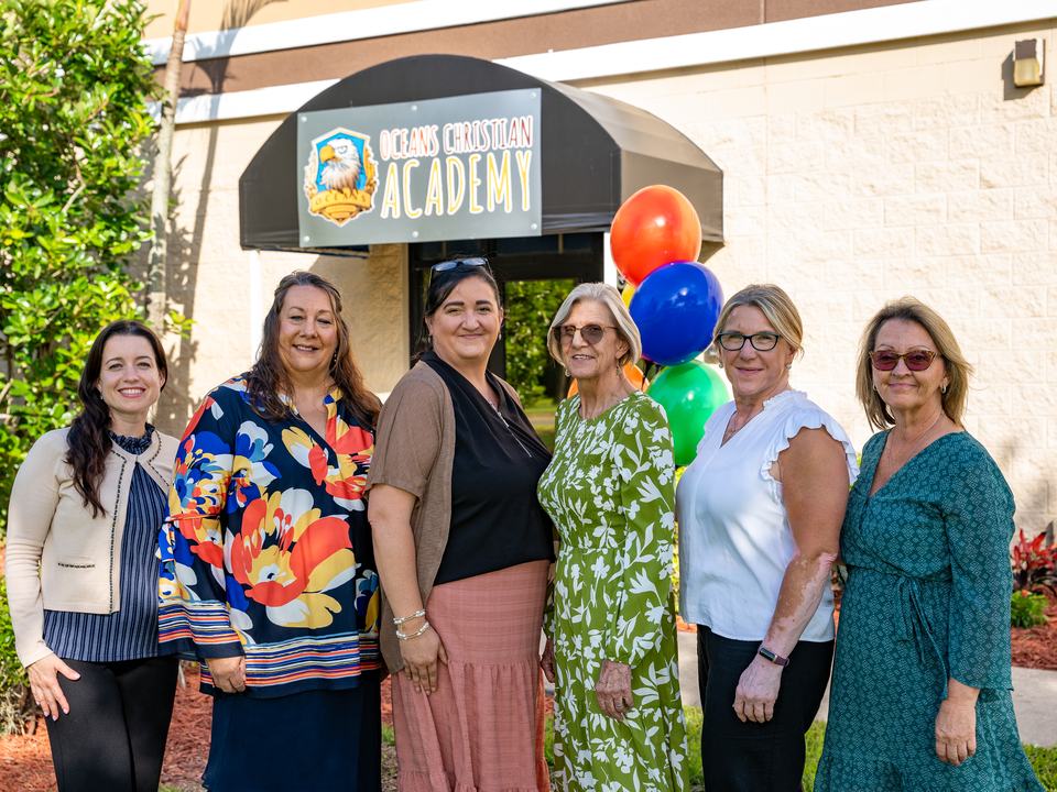 The OCA staff standing together outside the school entrance with balloons